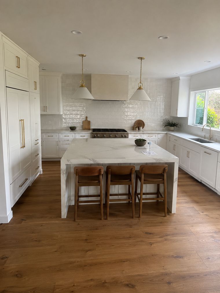 White kitchen with a marble waterfall island, brass pendants and wide-plank oak floor