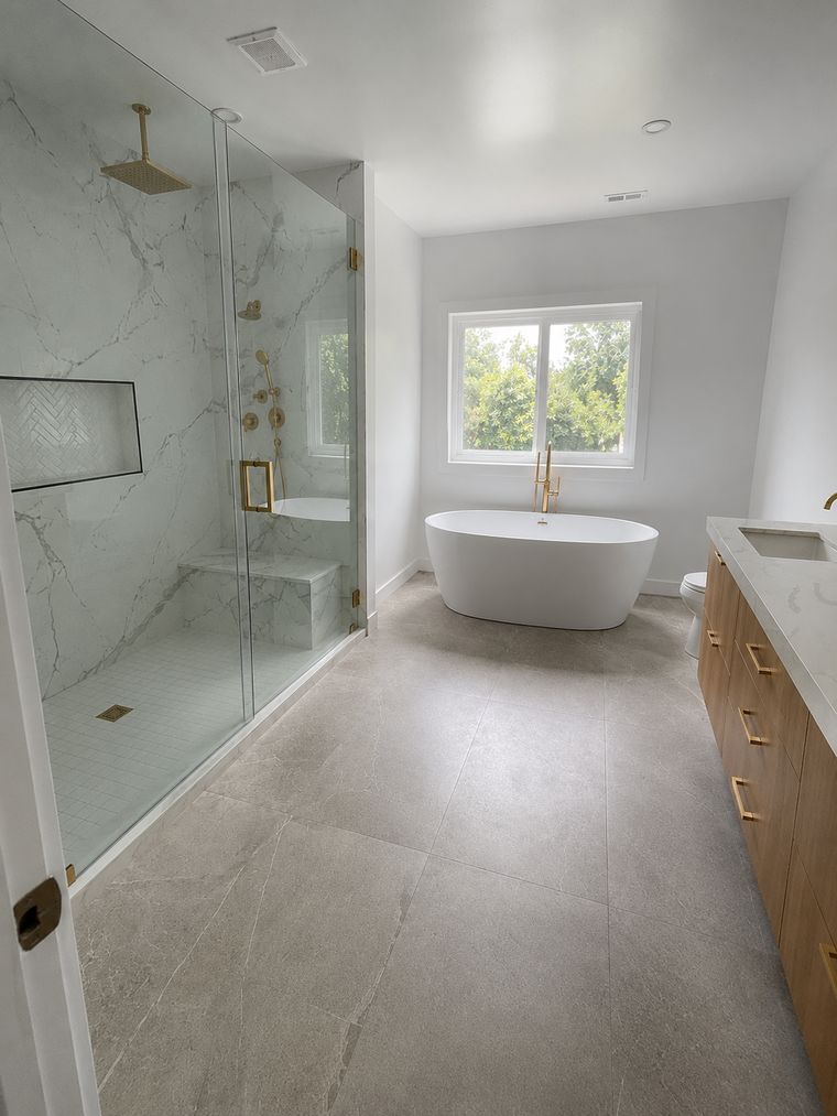 Primary bathroom with a curbless glass shower, freestanding tub and oak vanity